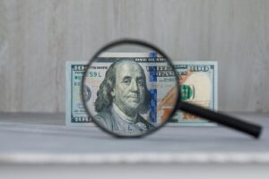 Magnifying glass dollar banknote grey wooden table 1024x683